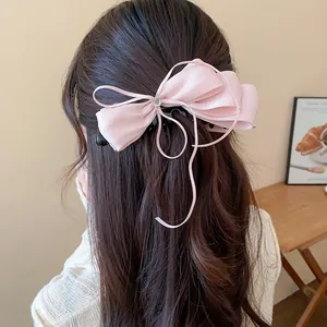 Close-up detail of a soft pink chiffon bow banana clip worn on wavy brown hair