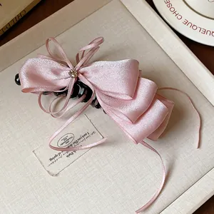 Detailed view of pink satin ribbon bow banana hair clip on a beige textured tray