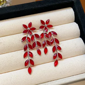 Close-up of red glass flower and leaf tassel earrings on a luxury cream jewelry tray.