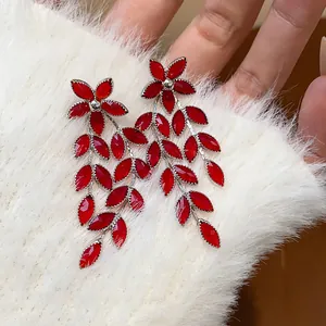 Close-up of elegant red glass flower and leaf tassel earrings on white faux fur background.