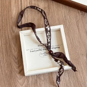 Gros plan d'un collier élégant en tissu à motifs marron avec une perle décorative