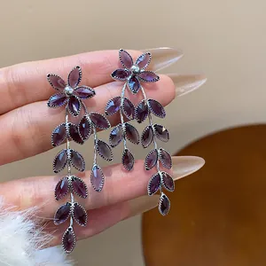 Detailed macro view of purple floral and leaf tassel earrings with silver needle posts.
