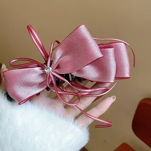 Close-up of an elegant pink satin bow banana hair clip with a sparkling central rhinestone ornament