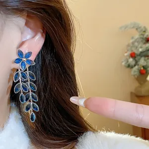 Detailed macro shot of elegant blue glass flower and leaf tassel earrings worn by model