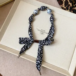 Détail rapproché du collier écharpe en soie léopard avec des perles marbrées grises