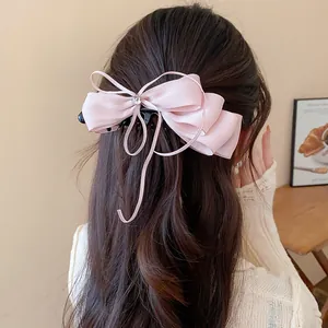 Detailed view of a pink chiffon bow ribbon banana hair clip on long brown wavy hair