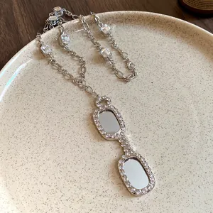 Detail view of a silver-toned necklace featuring an eyewear-shaped zircon pendant