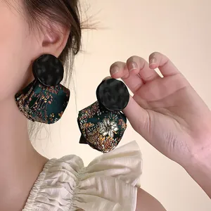 Close-up of retro New Chinese style earrings with wooden studs and green brocade pendants.