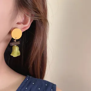 Detail view of a retro wooden pendant earring with green resin stone on an Asian model