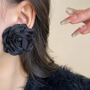 Close-up of a chic oversized black fabric rose flower earring on a model's ear detail view