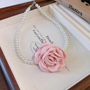 Close-up detail of an elegant pink fabric rose flower and white pearl beaded choker necklace