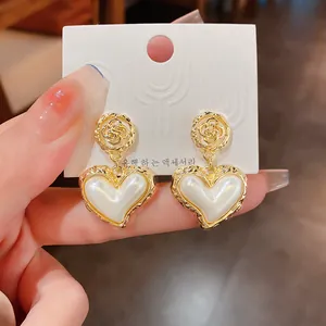Vue détaillée d'élégantes boucles d'oreilles cœur dorées avec incrustation perle.