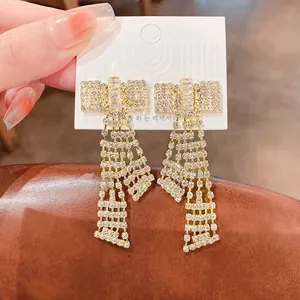 Vue détaillée de boucles d'oreilles nœud papillon à pompons dorés et cristaux étincelants