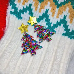 Festive colorful Christmas tree stud earrings with gold star accents on winter knit background.