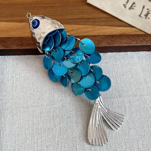Macro view of a metallic fish charm featuring blue iridescent scales and a nazar eye bead.