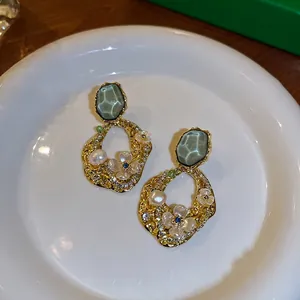 Eleganti orecchini geometrici dorati vintage con perle e dettagli floreali su piatto bianco