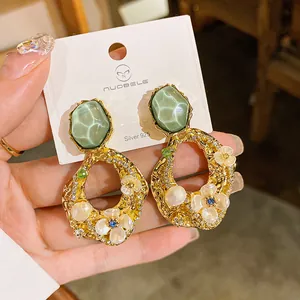 Dettaglio di orecchini vintage dorati con pietre verdi, perle e motivi floreali.