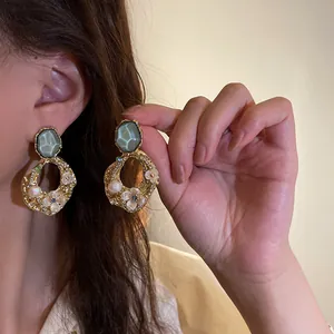 Dettaglio di orecchini geometrici dorati con perle e raffinato design floreale.