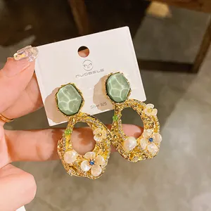 Dettaglio degli orecchini floreali in oro con perle e sfaccettature verdi