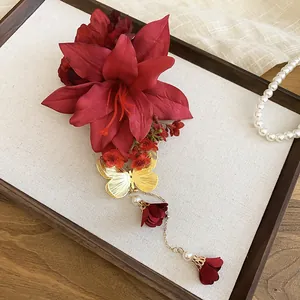 Close-up of a red lily hair clip with golden butterfly and pearl tassels on a display board.