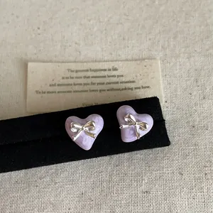 Detailaufnahme von violetten Herzohrringen mit silberner Schleife auf schwarzem Ständer