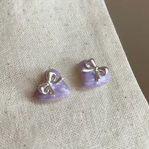 Detailansicht eleganter lila herzförmiger Ohrstecker mit einer silbernen Schleifenverzierung