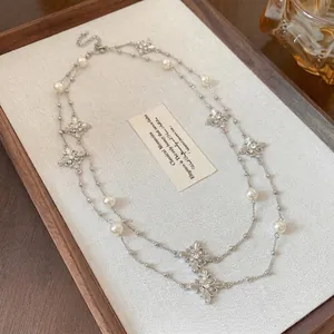 Double-layered cross necklace with pearls and rhinestones on a beige background.