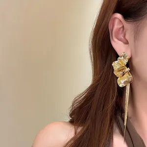 Dettaglio di eleganti orecchini a nappa con petali dorati indossati da una modella