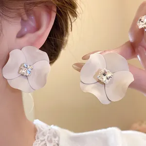Close-up of elegant matte white flower earrings with square rhinestone center