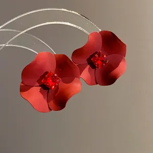 Close-up detail of red matte flower stud earrings with a sparkling red crystal center