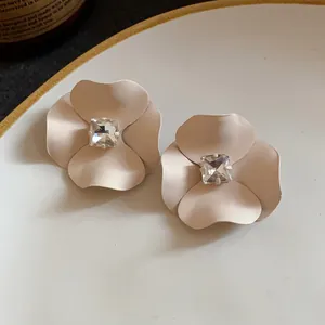 Detailed close-up of matte nude flower stud earrings featuring a sparkling square rhinestone