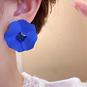 Close-up of matte blue flower earring with dark blue rhinestone on ear