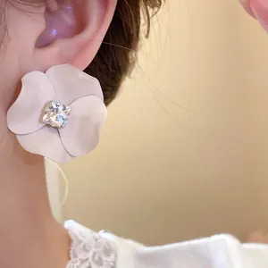 Macro view of a white matte flower stud earring featuring a square crystal center piece.