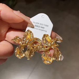 Detail shot of oversized gold-toned iris flower stud earrings with detailed metallic petals