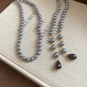 Detail view of a long grey pearl necklace with teardrop pendants on a vintage book