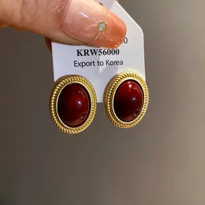 Detail view of vintage-style oval earrings with deep red stones and gold textured borders