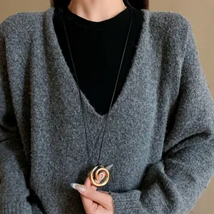 Primo piano di una collana con ciondolo a spirale dorata su uno sfondo grigio.