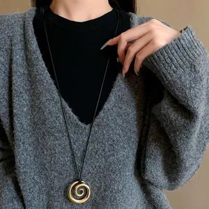 Primo piano di una collana con ciondolo a spirale dorata su cordoncino nero indossata.