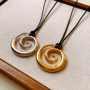 Dettaglio macro dei pendenti a spirale oro e argento su cordoncini neri minimalisti