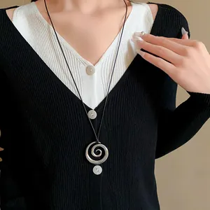 Primo piano della collana con ciondolo a spirale d'argento su un maglione bianco e nero