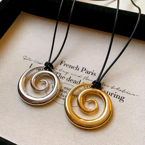 Dettaglio di ciondoli a spirale in metallo oro e argento su cordini neri su tela.