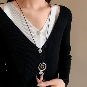 Dettaglio ravvicinato di una collana con ciondolo a spirale in metallo argento e corda