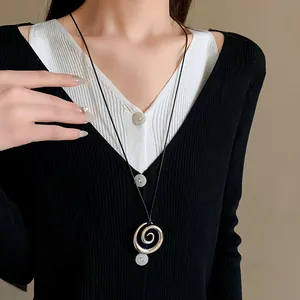 Primo piano di una collana con ciondolo a spirale argento indossata su un maglione.