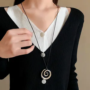 Primo piano di una collana con ciondolo a spirale argento su un maglione nero