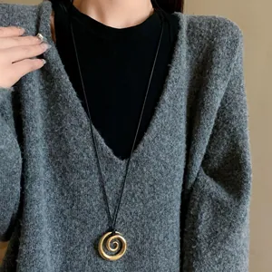 Dettaglio di una collana con ciondolo a spirale dorato indossata su un maglione grigio