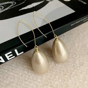 Close-up of elegant French style teardrop pearl earrings with golden curved hooks.