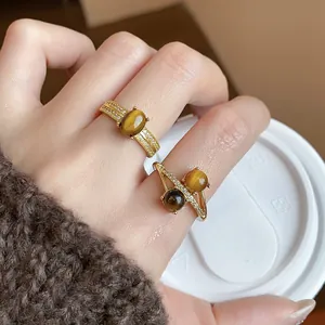 Close-up of 18k gold plated tiger eye rings with zircon on finger holding a cup.