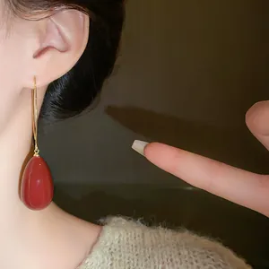 Close-up of elegant red teardrop earring with gold hook worn on ear