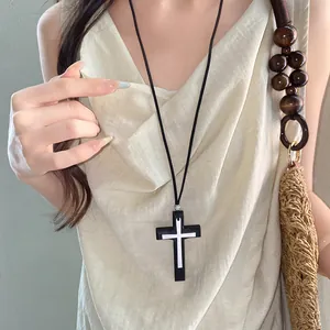 Primo piano della collana con pendente a croce nera vintage su lungo cordino in pelle su modella