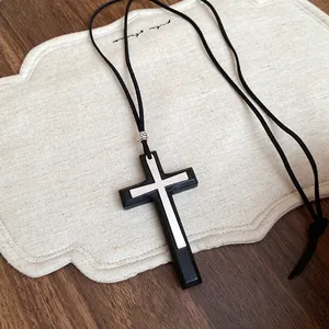 Dettaglio del ciondolo a croce nera con inserto argento su lunga collana in cuoio